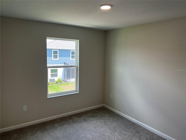unfurnished room with dark colored carpet, baseboards, and a textured ceiling