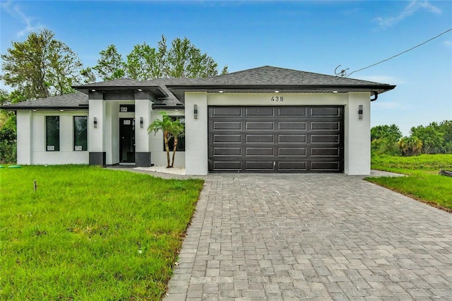 prairie-style house with a shingled roof, a garage, stucco siding, a front yard, and decorative driveway