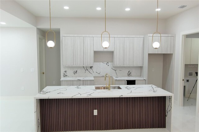 kitchen featuring pendant lighting, a kitchen island with sink, modern cabinets, tasteful backsplash, and a sink
