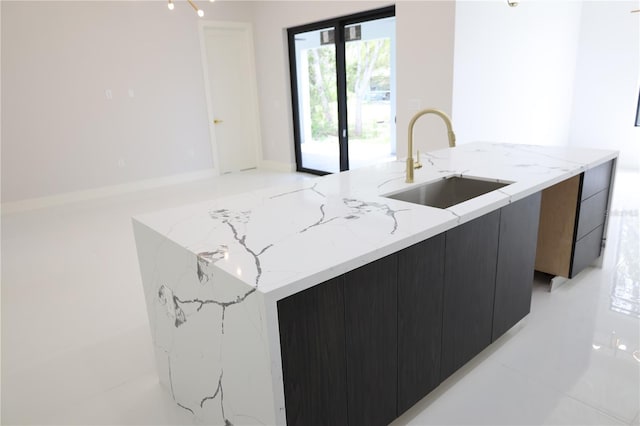 kitchen with light stone countertops, a sink, dark cabinetry, an island with sink, and modern cabinets