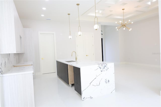 kitchen featuring a kitchen island with sink, modern cabinets, a sink, coffered ceiling, and decorative light fixtures