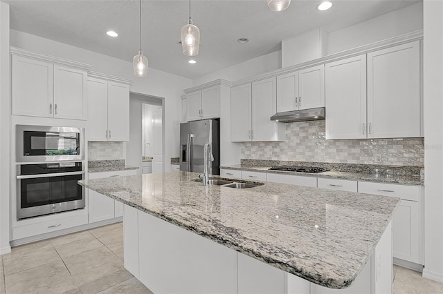 kitchen with stainless steel appliances, a sink, under cabinet range hood, white cabinets, and a center island with sink