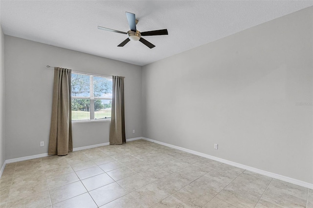 empty room with ceiling fan, light tile patterned floors, baseboards, and a textured ceiling