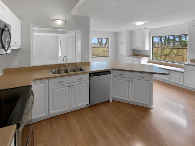 kitchen featuring light wood-style floors, light countertops, white cabinetry, a sink, and appliances with stainless steel finishes