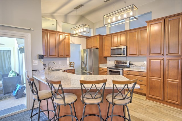 kitchen featuring appliances with stainless steel finishes, a sink, brown cabinetry, a peninsula, and high vaulted ceiling