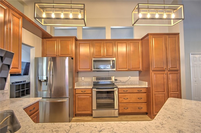 kitchen with appliances with stainless steel finishes, light stone counters, brown cabinets, light wood-style flooring, and decorative light fixtures