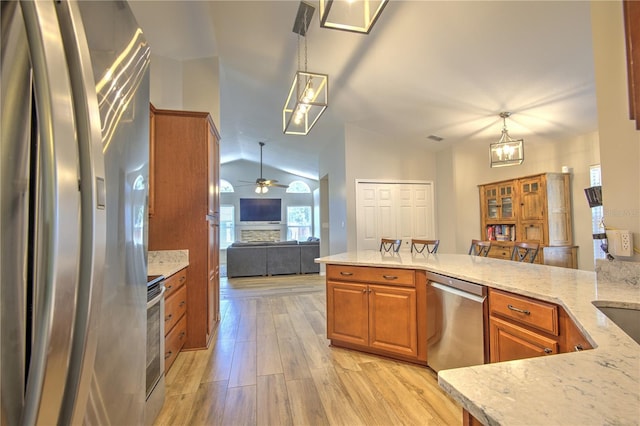 kitchen with stainless steel appliances, brown cabinetry, light wood-style flooring, open floor plan, and light stone counters