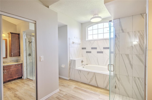 bathroom featuring a shower stall, vanity, a bath, wood finished floors, and a textured ceiling