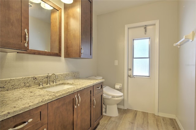 bathroom featuring wood finished floors, toilet, vanity, and baseboards
