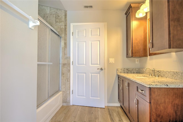 full bath featuring wood finished floors, vanity, and combined bath / shower with glass door