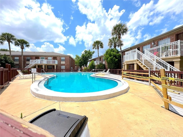 community pool with stairs, a patio area, and fence
