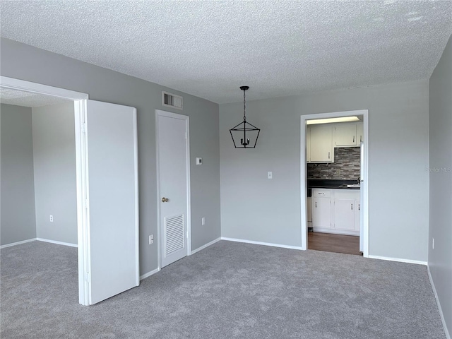 empty room featuring a textured ceiling, baseboards, visible vents, and dark carpet