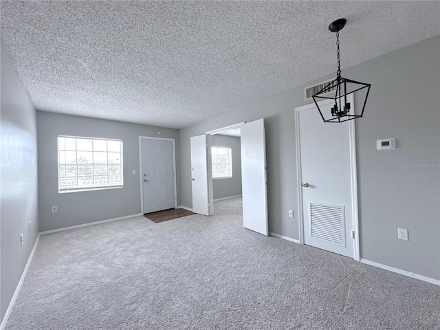 interior space featuring a textured ceiling, carpet, visible vents, a chandelier, and baseboards