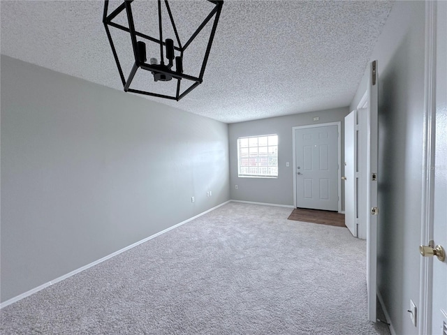 empty room featuring a chandelier, a textured ceiling, carpet floors, and baseboards