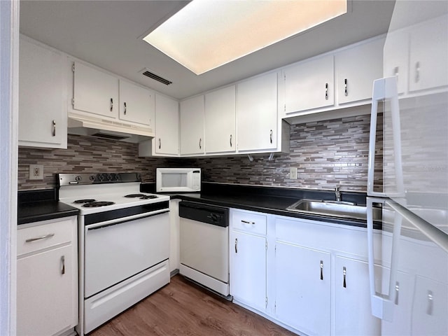 kitchen with under cabinet range hood, dark countertops, visible vents, and white appliances