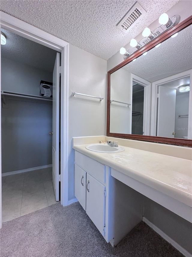 bathroom with a textured ceiling, visible vents, tile patterned floors, vanity, and a spacious closet
