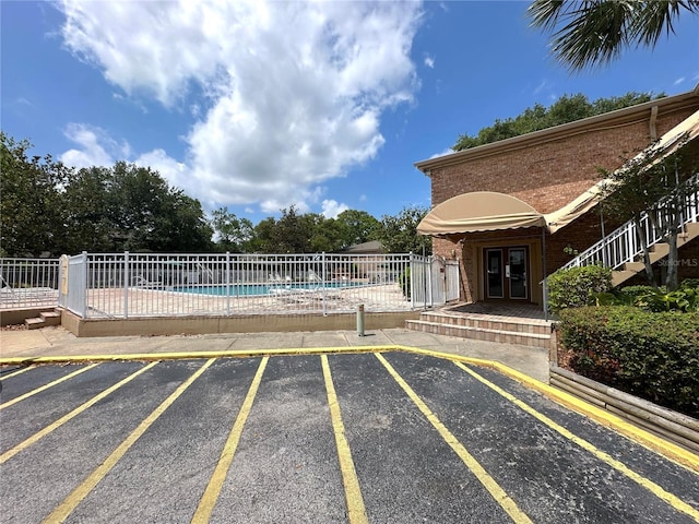 uncovered parking lot with french doors, a community pool, and fence