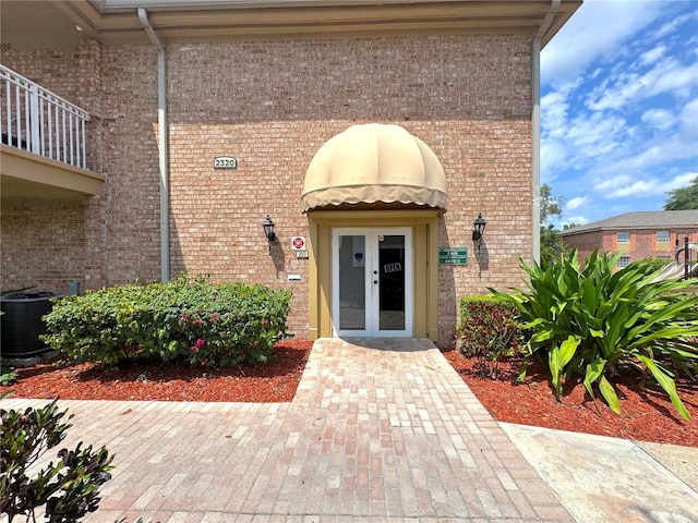 entrance to property with central AC unit, french doors, and brick siding