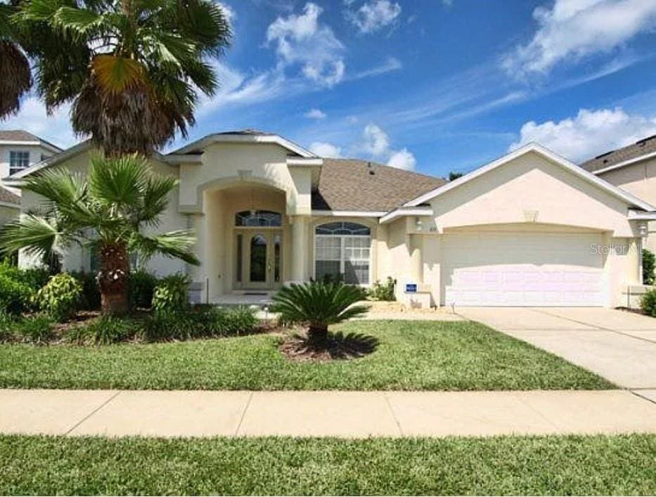view of front facade with a garage, a front yard, stucco siding, french doors, and driveway