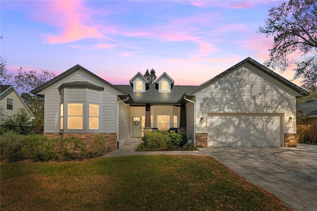 view of front of house with a lawn, an attached garage, driveway, and stone siding