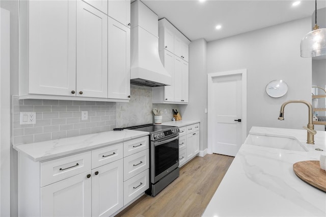 kitchen with a sink, premium range hood, white cabinets, light wood finished floors, and electric stove