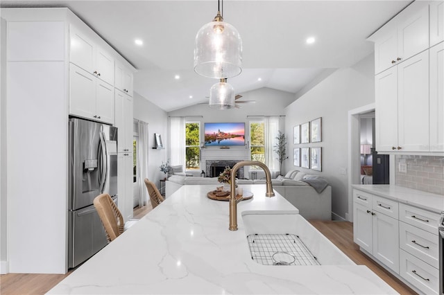 kitchen featuring open floor plan, vaulted ceiling, stainless steel fridge, and a fireplace