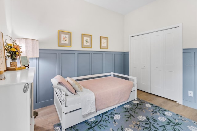 bedroom with a closet, a decorative wall, wainscoting, and light wood-type flooring