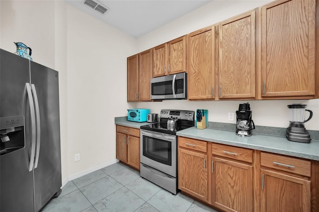 kitchen featuring visible vents, brown cabinetry, light countertops, light tile patterned floors, and stainless steel appliances