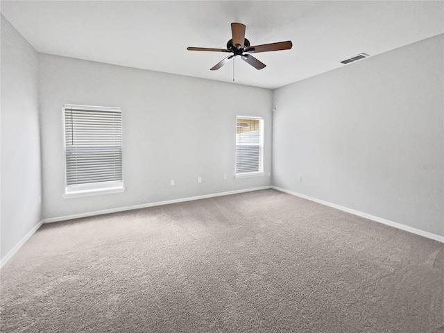 carpeted empty room with baseboards, a ceiling fan, and visible vents