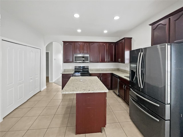 kitchen featuring arched walkways, appliances with stainless steel finishes, light tile patterned floors, and a kitchen island