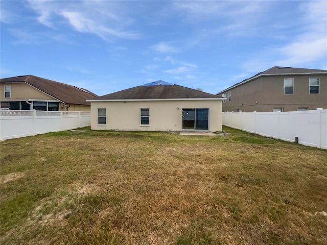 rear view of house featuring a fenced backyard, stucco siding, and a yard