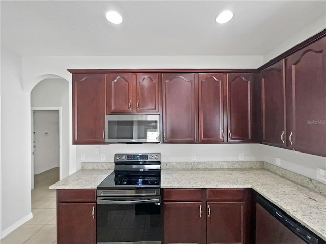 kitchen featuring dark brown cabinets, light stone counters, arched walkways, light tile patterned floors, and stainless steel appliances