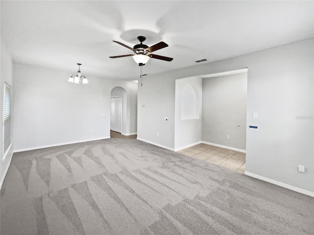 tiled spare room featuring visible vents, arched walkways, baseboards, carpet floors, and ceiling fan with notable chandelier