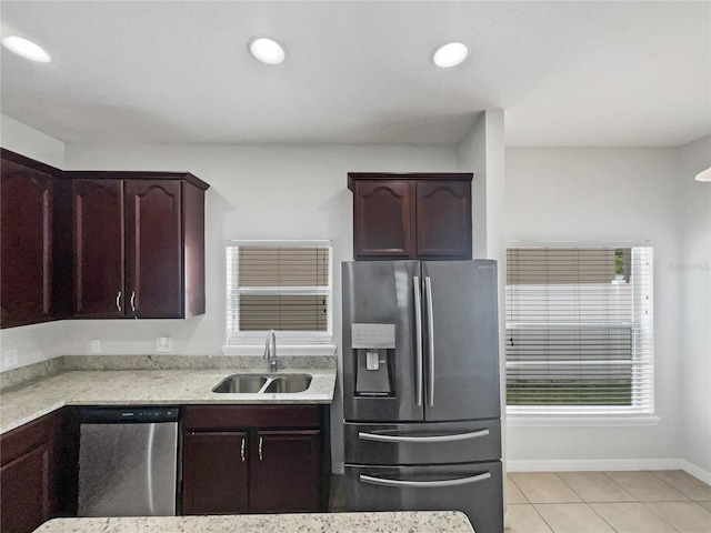 kitchen with appliances with stainless steel finishes, light stone counters, a sink, baseboards, and light tile patterned floors