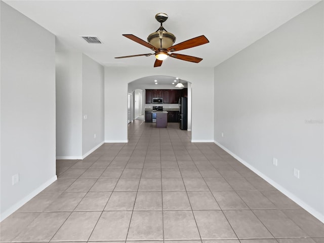 spare room featuring light tile patterned flooring, arched walkways, a ceiling fan, baseboards, and visible vents