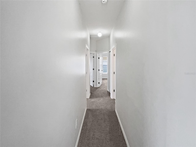 hallway with baseboards and dark carpet