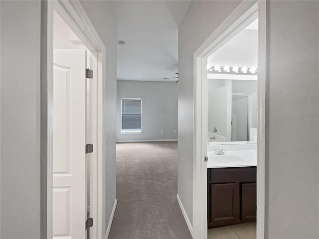 hall with light colored carpet, a sink, and baseboards
