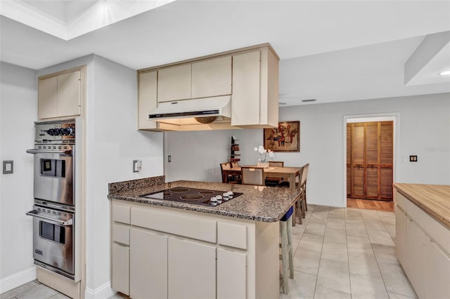 311 Needles Trl, Longwood, FL 32779 - kitchen with stainless steel double oven, black electric stovetop, cream cabinetry, under cabinet range hood, and baseboards