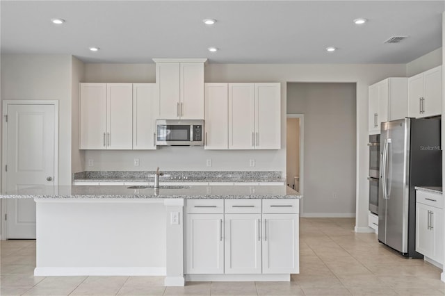 kitchen with light stone countertops, a sink, white cabinets, stainless steel appliances, and an island with sink