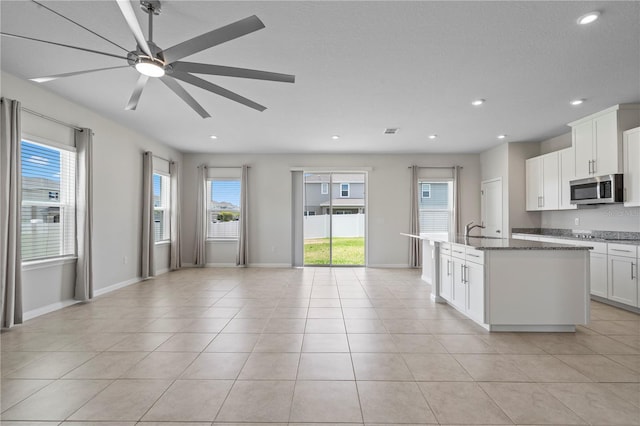 kitchen with a sink, dark stone counters, a ceiling fan, stainless steel microwave, and open floor plan