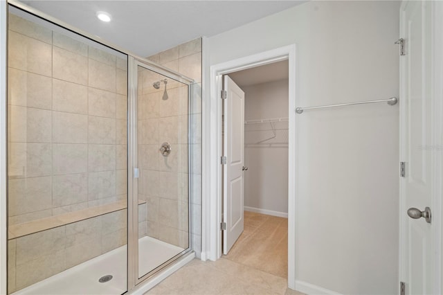 full bathroom with tile patterned floors, a spacious closet, baseboards, and a stall shower