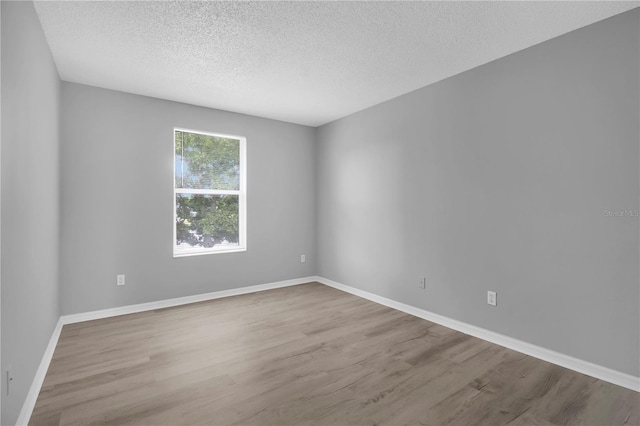 spare room featuring a textured ceiling, wood finished floors, and baseboards