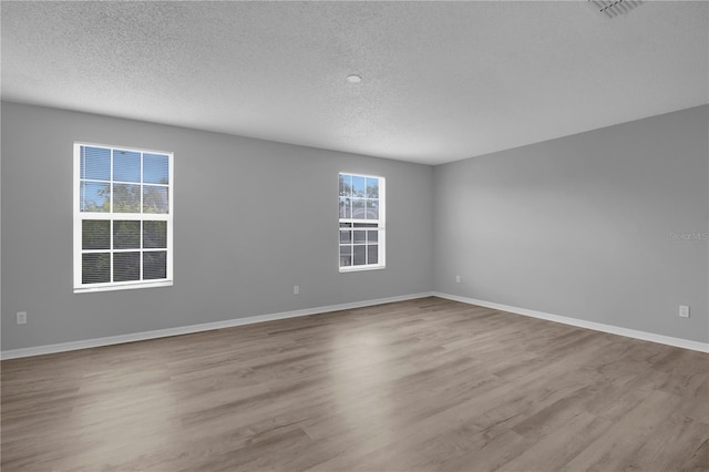 spare room featuring a textured ceiling, baseboards, visible vents, and wood finished floors