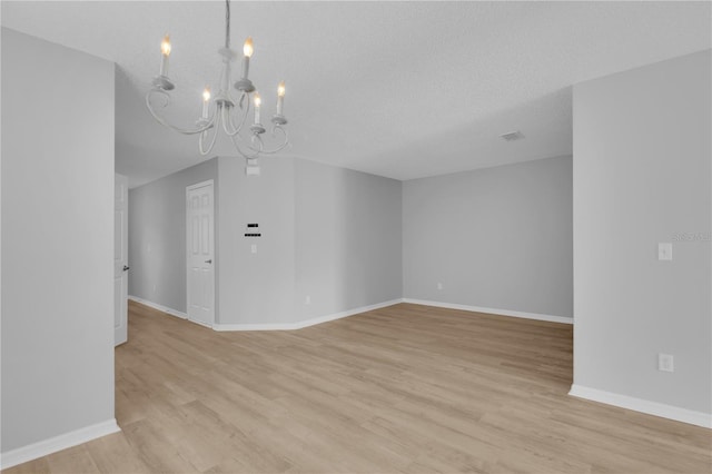 spare room with a chandelier, light wood finished floors, baseboards, and a textured ceiling