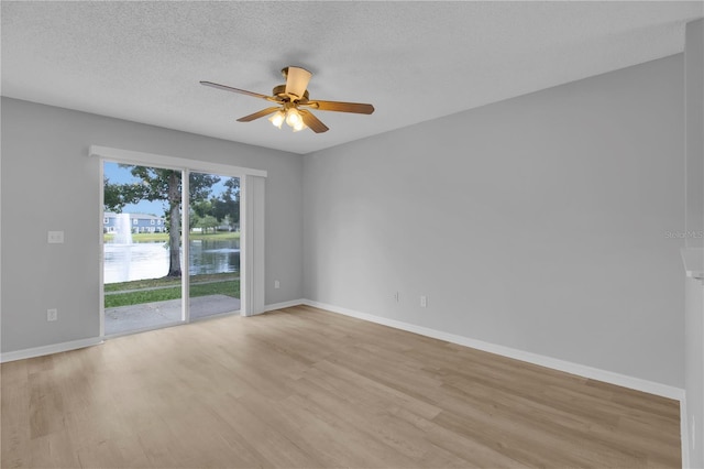 unfurnished room with light wood-style flooring, a water view, a ceiling fan, baseboards, and a textured ceiling