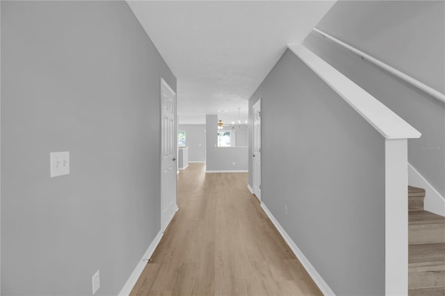 hallway with stairway, an inviting chandelier, baseboards, and light wood finished floors