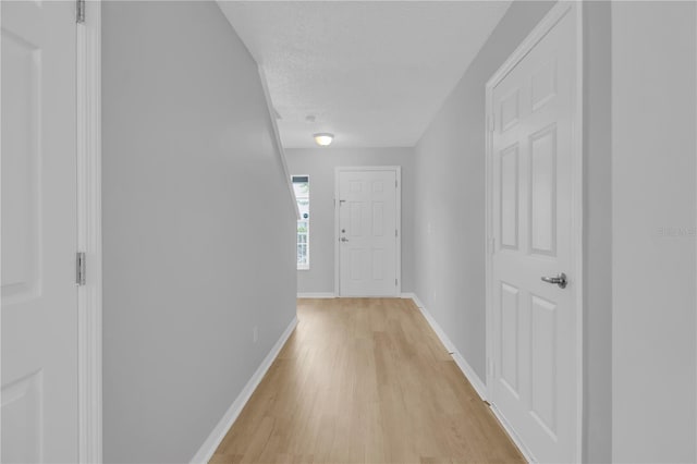 hallway featuring a textured ceiling, baseboards, and light wood-style floors