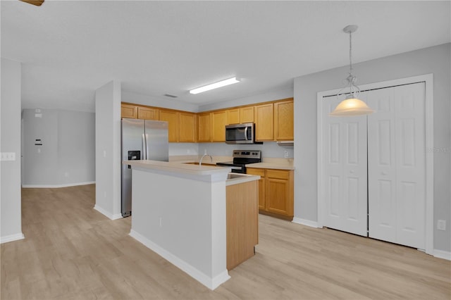 kitchen featuring stainless steel appliances, light wood finished floors, light countertops, an island with sink, and pendant lighting