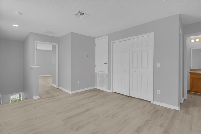 unfurnished bedroom featuring light wood finished floors, baseboards, a closet, and a textured ceiling