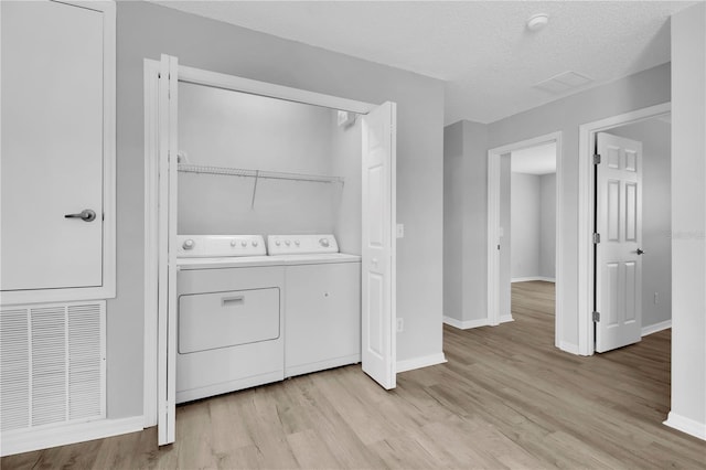 washroom with washer and dryer, light wood-type flooring, baseboards, and a textured ceiling